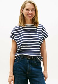 Camiseta de rayas marino y blanca de manga corta con cuello redondo y mangas enrolladas, combinada con vaqueros oscuros y un cinturón negro.