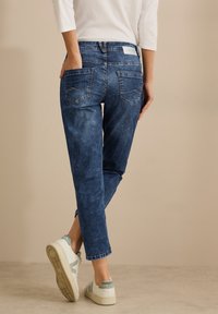 Jeans in denim blu chiaro, usurati, con una vestibilità rilassata, tasche posteriori e una texture leggermente sbiadita. Abbinati a sneakers bianche con accenti grigi.