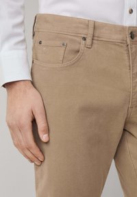 Beige katoenen chinos met een soepele textuur, voorzien van een voorzak, metalen knoopaccenten en subtiele stikdetails.