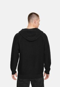 Felpa nera in maglia con finitura testurizzata, caratterizzata da una vestibilità comoda, maniche lunghe e cappuccio visibile, vista da dietro.