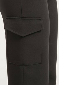 Pantalons cargo noirs en tissu texturé, avec poche latérale à rabat, coupe ajustée et coutures lisses pour une apparence épurée.