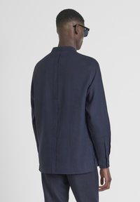 Camicia di lino blu navy con colletto alla cinese, maniche lunghe e polsini con bottoni. Presenta un design semplice ed è indossata in posizione eretta.