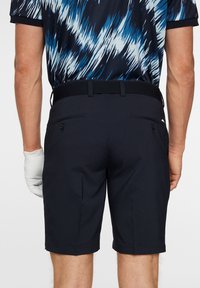 Navy Golf-Shorts mit geradem Schnitt, zwei Gesäßtaschen mit Knöpfen und einem elastischen Bund. Glatte Stoffoberfläche ohne sichtbare Muster.