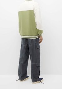 Groen en crèmekleurig sweatshirt met geribbelde manchetten en zoom, gecombineerd met loszittende grijze cargobroek met meerdere zakken.