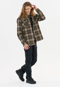 Geruite shirt in aardetinten van bruin en beige, met twee borstzakken en een relaxte pasvorm, gecombineerd met zwarte cargobroek en zwarte sneakers.