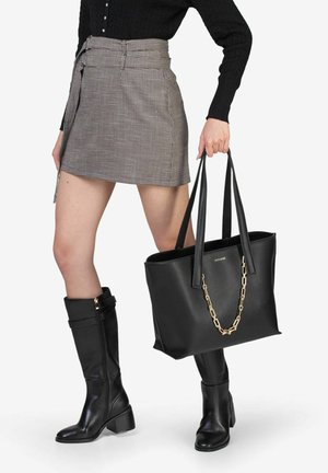 Borsa tote in pelle nera con riflessi in catena dorata, design elegante, manici robusti, interno spazioso, abbinata a una gonna a scacchi e stivali fino al ginocchio.