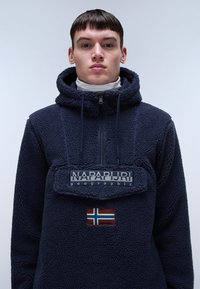 Pullover in pile blu navy con cappuccio, dotato di zip frontale, patch con logo e dettaglio della bandiera della Norvegia sul petto.