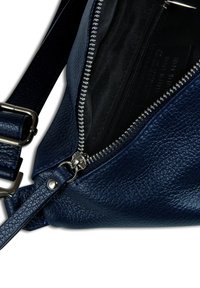 Sac bandoulière en cuir bleu marine avec surface texturée, fermeture éclair argentée et bandoulière ajustable. L'intérieur est doublé de noir et comprend une poche zippée.