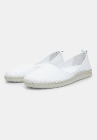 Zapatos planos de piel blanca sin cordones, con puntera redondeada, costuras texturizadas a lo largo de la suela y un suave forro interior.