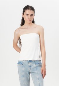 Hvit ribbet strapless topp med sideknapper, myk tekstur og rett snitt. Kombinert med lys blå tettsittende jeans.