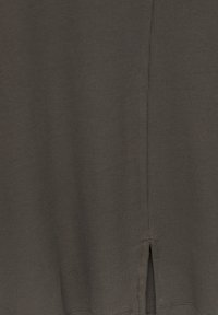 Top en tissu côtelé gris foncé avec une fente sur le côté au bas. Détail de couture visible à l'ourlet. Texture lisse et coupe ajustée.
