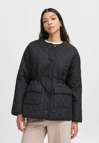 Gep quiltete schwarze Jacke mit Druckknöpfen, tailliertem Design und zwei Fronttaschen. Weicher Stoff, abgerundeter Ausschnitt und lässige Passform.