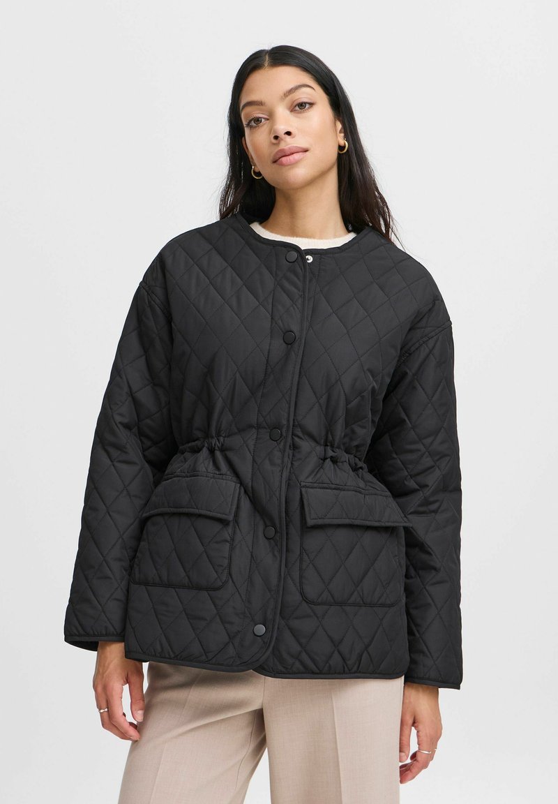 Gep quiltete schwarze Jacke mit Druckknöpfen, tailliertem Design und zwei Fronttaschen. Weicher Stoff, abgerundeter Ausschnitt und lässige Passform.