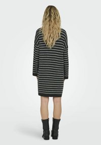 Vestido de punto con mangas largas, con rayas horizontales en gris y negro. Textura suave, corte relajado, cae por encima de las rodillas, combinado con botas negras.