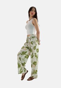 Lichte, groene en beige bloemenpatroon wijdlopende broek met een elastische tailleband. G gedragen met een witte crop top en bruine sandalen.