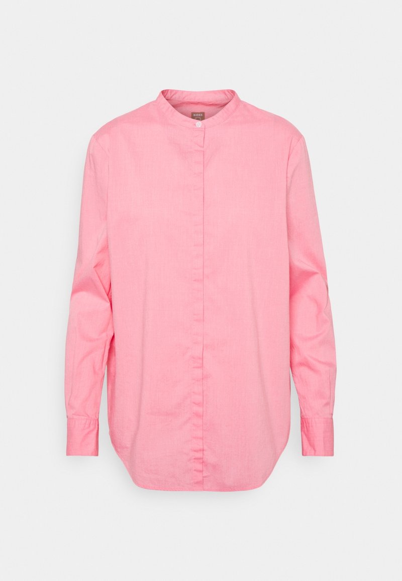 Chemise rose à manches longues avec boutons, col mao et boutons cachés, présentée sur fond clair uni.