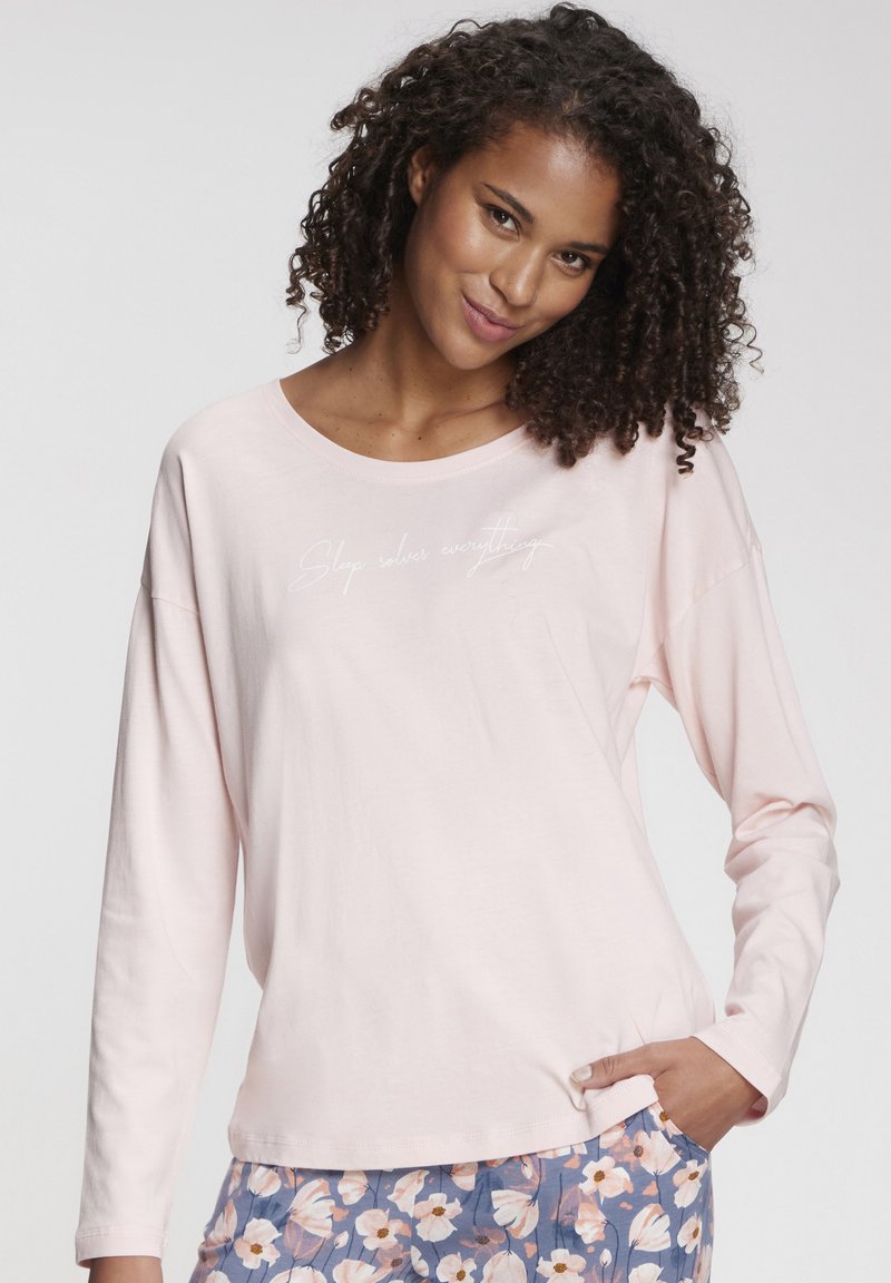 Light pink long-sleeve top with a rounded neckline and embroidered text. Soft fabric and relaxed fit, paired with patterned floral bottoms.