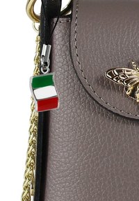 Lichtpaarse leren handtas met een gouden kettingriem, voorzien van een vlinderaccent en een klein Italiaans vlaggetje charm eraan bevestigd.