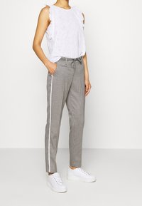 Biała haftowana bluzka z falbanami na rękawach, w połączeniu z szarymi spodniami w kratę z boczną prążkowaną wstawką i białymi trampkami.