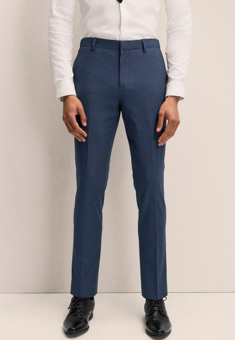 Blaue maßgeschneiderte Hosen mit glatter Textur, schlankem Design und Gürtelschlaufen, kombiniert mit schwarzen formellen Schuhen. Klassische Stilmerkmale sind vorhanden.