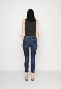 Mörkblå denim skinny jeans, mid-rise passform, femficksdesign, med minimal blekning, beskurna ovanför vristen, kombinerade med en svart tajt topp.