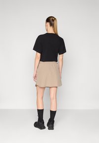 Camiseta negra de manga corta, falda beige con cintura elástica, calcetines negros y zapatos negros. Diseño minimalista, textura suave, apariencia casual.