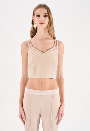 Top corto beige con scollo a V e due spalline; realizzato in tessuto liscio e strutturato. Presenta dettagli di cuciture sul davanti.