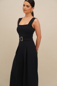 Μπλε ναυτικού χρώματος ολόσωμη φόρμα με τετράγωνο ντεκολτέ, φαρδιές τιράντες, εφαρμοστή μέση με ορθογώνια ζώνη και πλισέ παντελόνια με φαρδιά μπατζάκια.