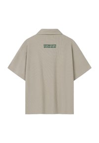 Polo beige à manches courtes avec col et texte vert dans le haut du dos indiquant "TOUT EST MEILLEUR AVEC LA PAIX ET L'AMOUR."
