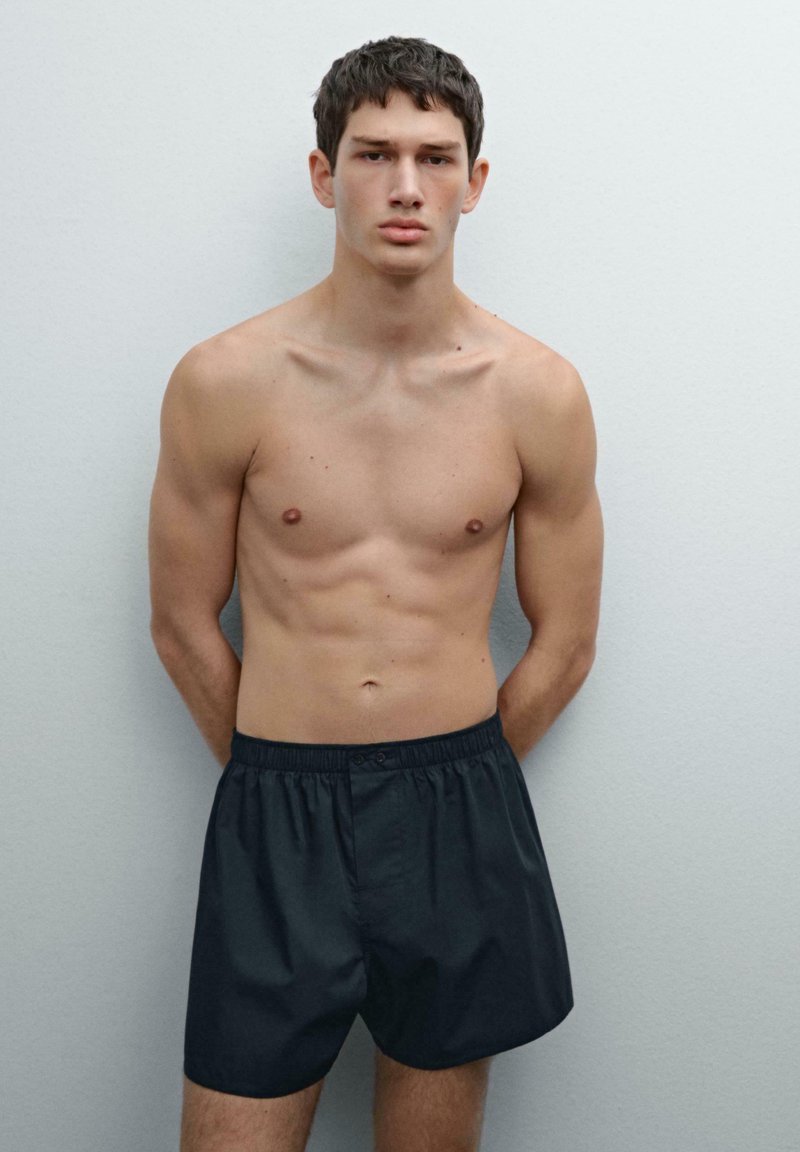 Shorts de bain noirs en tissu léger, dotés d'une taille élastique et d'une fermeture à un bouton, présentés sur un modèle.