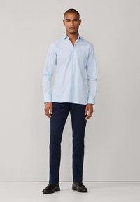 Camisa azul claro abotonada, pantalones azul marino y zapatos oscuros. La camisa presenta un cuello clásico y mangas largas, con una textura de tela suave.