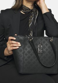 Schwarze Leder-Tote-Tasche mit geprägtem Blumenmuster, silbernen Beschlägen, doppelten Tragegriffen und einem Schloss-Detail. Glatte Textur und strukturierte Form.