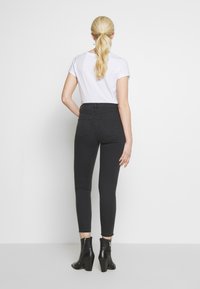 Jeans negros de cintura alta con un ajuste ajustado, que cuentan con dos bolsillos traseros y un ligero desgastado, combinados con botas negras hasta el tobillo y una camiseta blanca.
