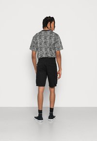 Schwarzes und weißes kurzärmliges Musterhemd mit lockerer Passform, kombiniert mit schwarzen Cargo-Shorts mit Seitentaschen und einer einheitlichen Textur.