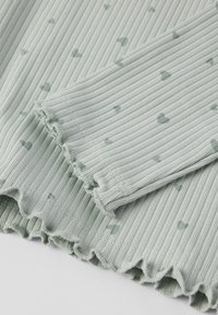 Vaaleanvihreä ribbikangas, jossa on pieniä harmaita sydämiä, ja se esittelee lettireunuksen yksityiskohtia hihoissa ja helmassa.