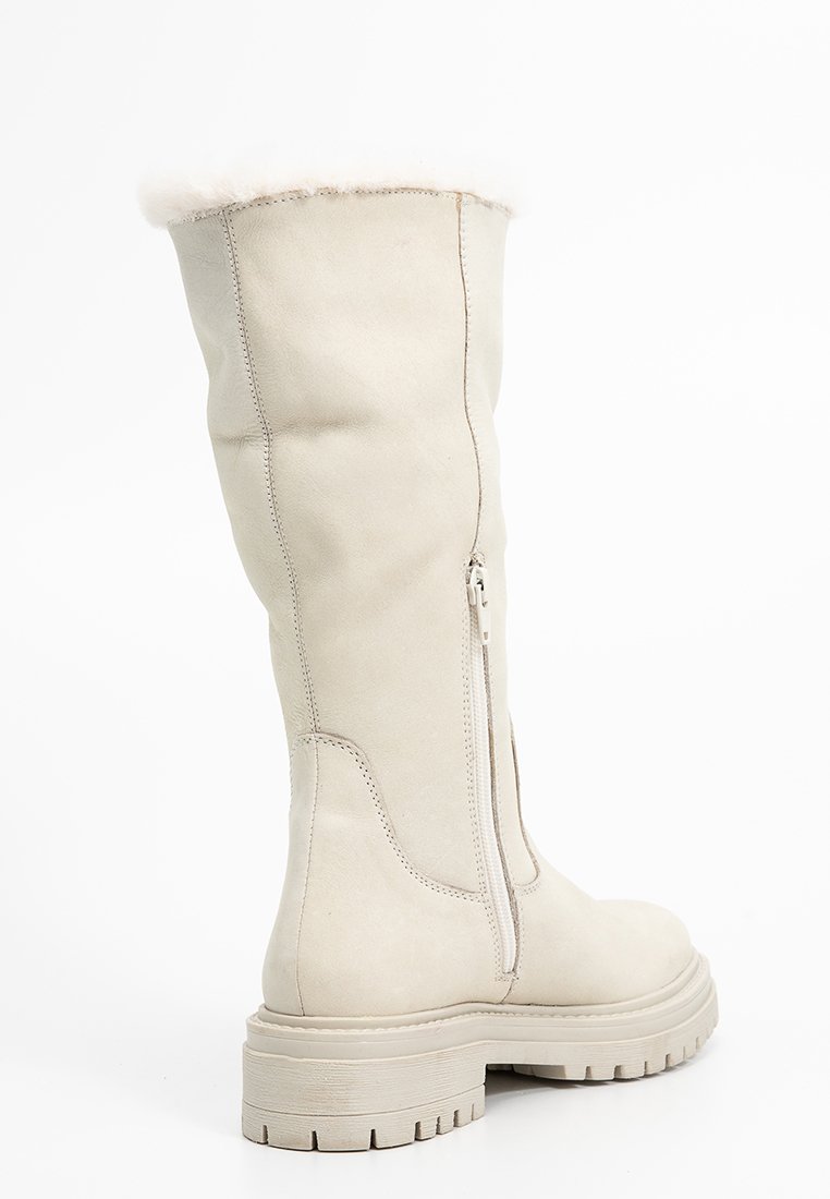 Botte en cuir beige arrivee genoux avec doublure en fausse fourrure, fermeture éclair latérale, semelle épaisse et surface légèrement texturée. Forme angulaire et peu de détails.