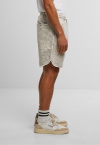 Shorts gris clair avec une texture, dotés d'une taille élastique et de deux poches latérales. Associés à des baskets blanches et des chaussettes rayées.