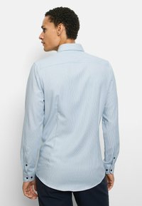 Light blue long-sleeve shirt with a subtle striped pattern, button cuffs, and a curved hem. Made of lightweight fabric.