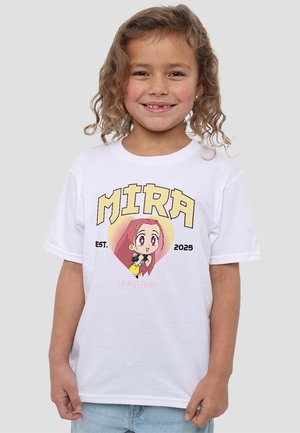 Lächelndes junges Mädchen mit lockigem Haar, das ein weißes T-Shirt mit einem Cartoon-Charakter, dem Text "MIRA EST. 2025" und hellblauen Jeans trägt.