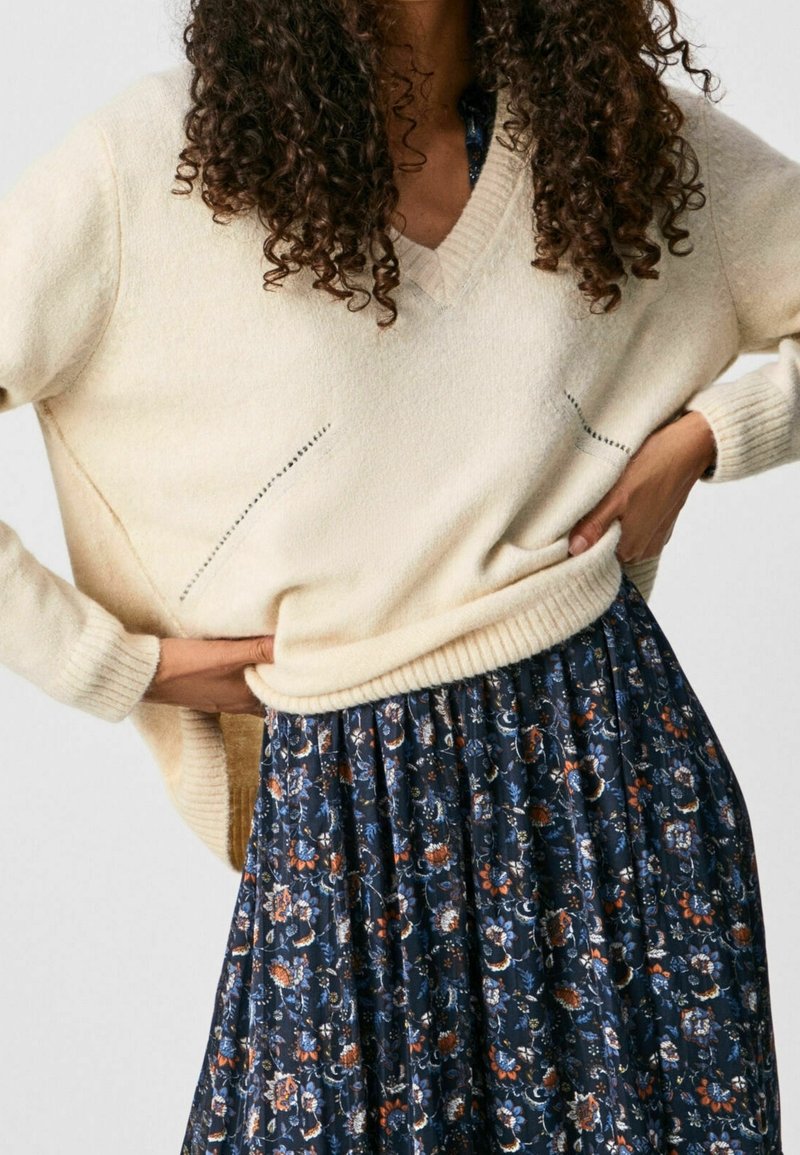 Cream-colored knitted sweater with a V-neck, paired with a dark floral skirt featuring blue and orange patterns. Textured fabric, relaxed fit.