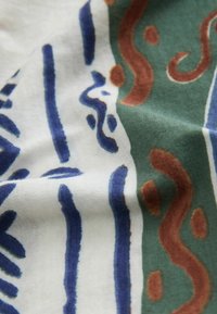 Tissu avec un fond vert, blanc et bleu présentant des motifs abstraits incurvés et linéaires en bleu et marron.