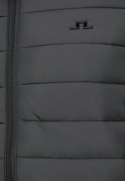 Casaco corta-vento puffer em cinza escuro com secções acolchoadas horizontais, fecho éclair de comprimento total e um detalhe de logo preto perto do peito. Textura suave.