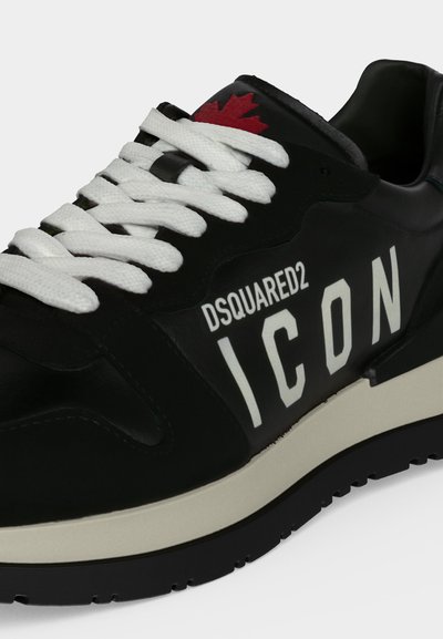 Baskets noires avec lacets blancs, semelle blanche, texte "DSQUARED2 ICON" sur le côté et une feuille d'érable rouge sur la languette.