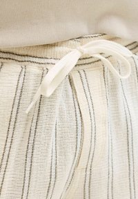 Κοντινό σε υφασμάτινη μέση με υφή, λεπτές κάθετες ρίγες και λευκό κορδόνι δέσιμο σε φιόγκο μπροστά.