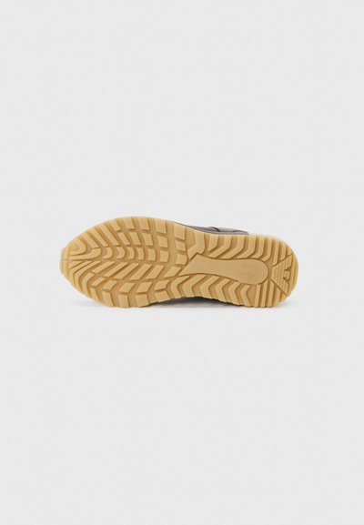Schwarze Schuhsohle mit einem strukturierten, gemusterten Profil. Die Sohle besteht aus Gummi mit einer beigen Zwischensohle und weist ein markantes Griffdesign auf.