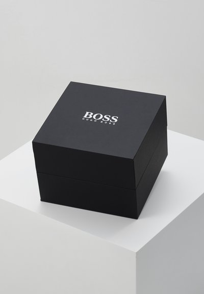 Boîte-cadeau carrée noire avec une finition lisse. Présente un logo blanc inscrit "BOSS HUGO BOSS" centré sur la surface supérieure.