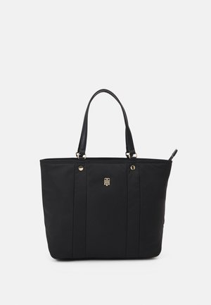 Sort tote taske med dobbelte håndtag, guldfarvet beslag og et lille gyldent logo centreret foran, sat mod en ensartet lys baggrund.