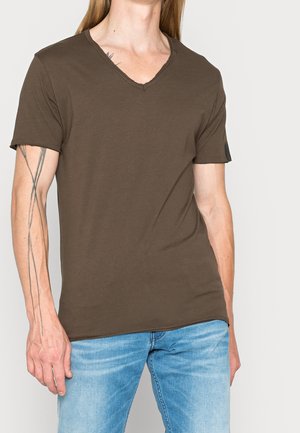 Brun bomulds V-hals t-shirt med kortærmer, der har en afslappet pasform og subtile syningsdetaljer. Kombineret med lyseblå jeans.