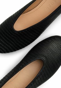 Scarpe nere basse in pelle strutturata, con punta arrotondata e design con ritagli. Fodera interna soffice beige visibile.
