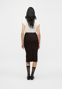 Καφέ ριμπ midi φούστα με εφαρμοστή σιλουέτα, συνδυασμένη με ανοιχτόχρωμο τοπ. Το μοντέλο φοράει διάφανα μαύρα καλτσάκια και μαύρα παπούτσια.